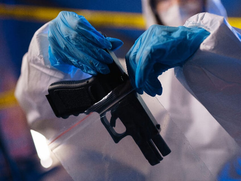 Close-up of criminologist in protective suit putting a gun in a plastic bag at the crime scene - stock photo