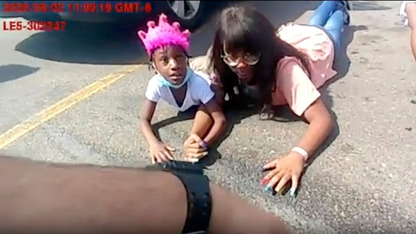 6-year-old Lovely Gilliam looks up at a police officer as she and her family members lie in a parking lot after they were wrongfully forced out of their car on Aug. 2, 2020, in Aurora, Colo. 