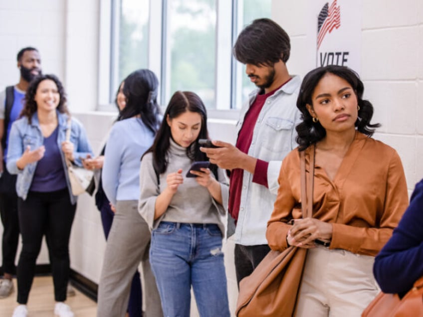 While waiting to vote, the multiracial group of people use their time to talk, look at social media on their smart phones, or just think.