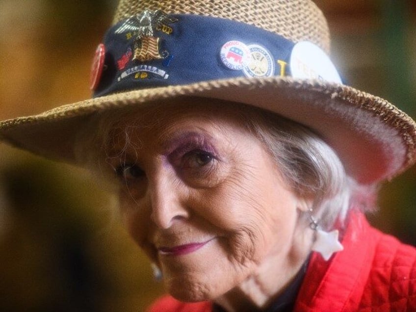 A woman wearing a hat with GOP supporting stickers smiles during a campaign rally for U.S.