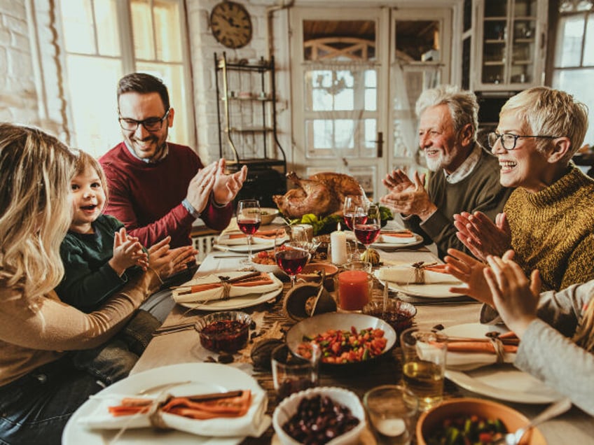 Happy multi-generation family clapping their hands while having Thanksgiving lunch in dini