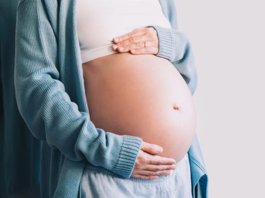 Pregnant woman holds hands on her belly.