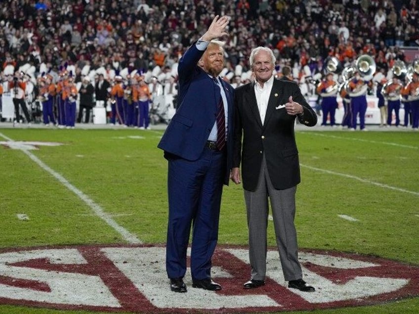 Republican presidential candidate and former President Donald Trump waves with South Carolina Gov. Henry McMaster during halftime in an NCAA college football game between the University of South Carolina and Clemson Saturday, Nov. 25, 2023, in Columbia, S.C. Trump has spent less time campaigning in early-voting states than many of …