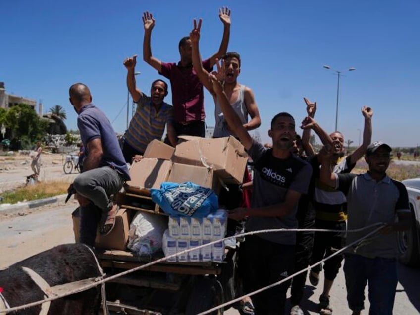 Palestinians wave to the camera as they carry boxes and bags containing food and humanitar