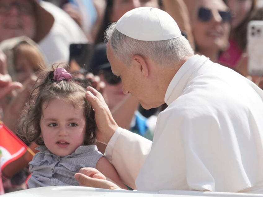 Pope Leo XIV caresses a child as he arrives for his weekly general audience in St. Peter&#