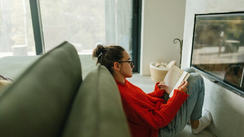 Woman reading a book by a fireplace