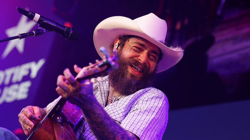 Musician Post Malone wears cowboy hat while playing the guitar.