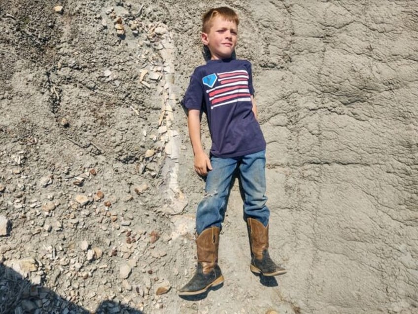 Young Liam Fisher lay down next to the fossilized leg bone of a dinosaur he discovered in