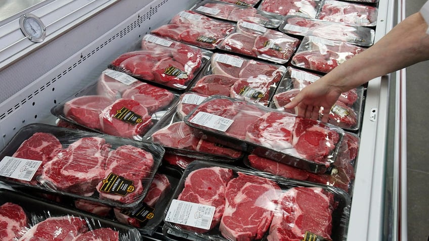 Customer's hand seen reaching for pack of steak among display case at grocery store