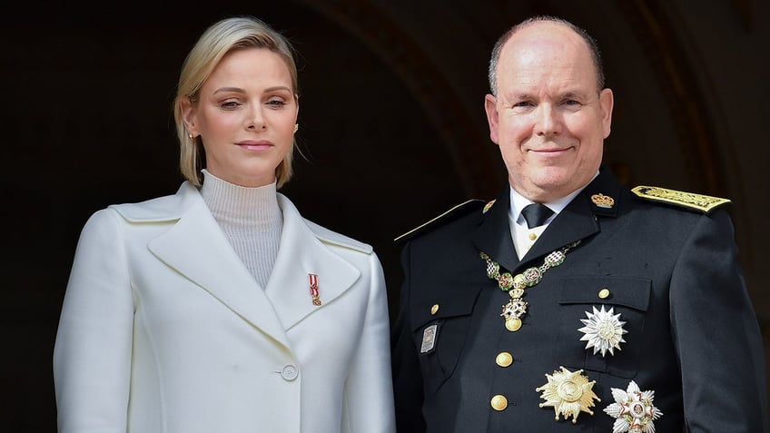 A close-up of Princess Charlene wearing white standing next to Prince Albert in a suit with medals