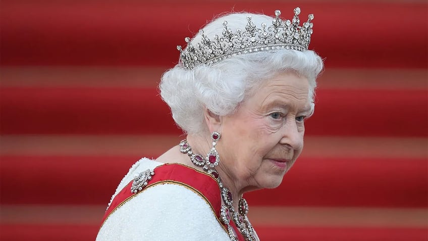 A close-up of Queen Elizabeth wearing a tiara and a red sash