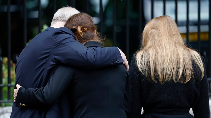 Prince Andrew embracing his daughters with their backs turned.