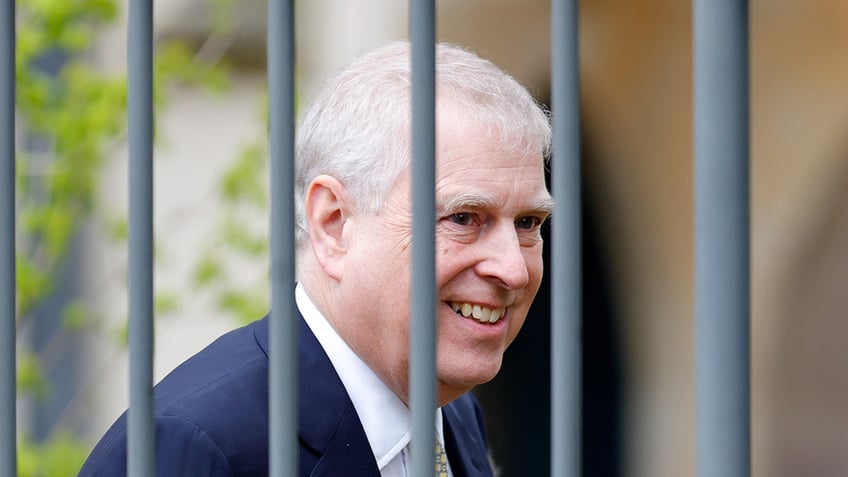 A close-up of Prince Andrew smiling in front of a fence.