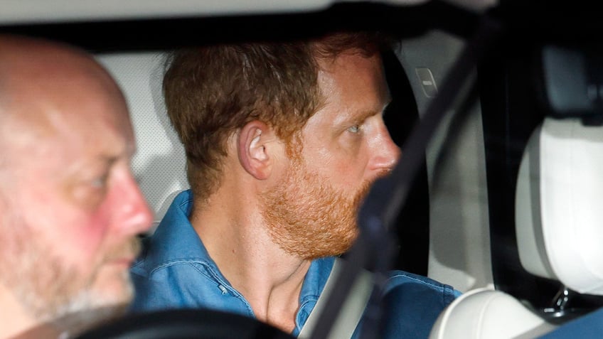 Prince Harry looking away as he sits inside a car.