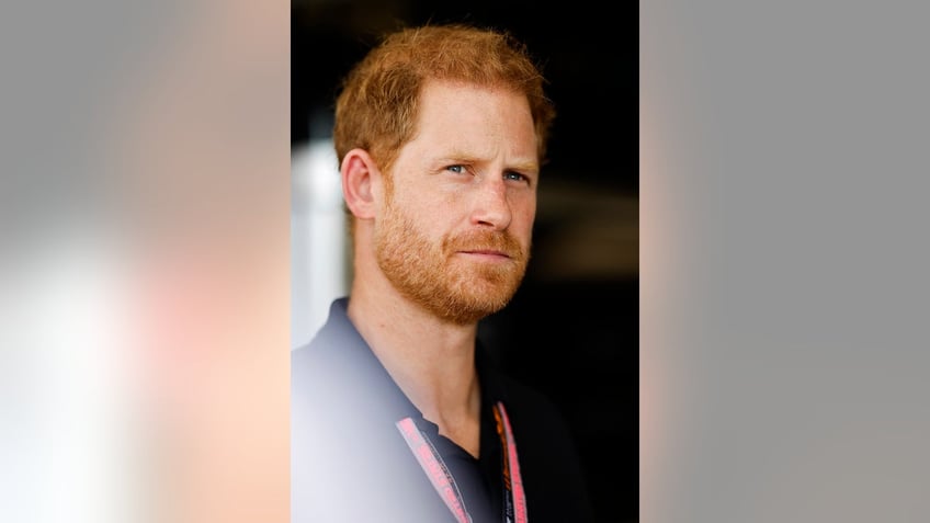 A close-up of Prince Harry looking up wearing a navy polo shirt.