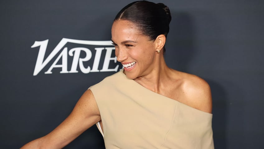 Meghan Markle smiling in a beige off-shoulder dress