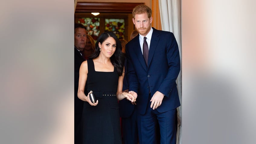 Prince Harry in a dark blue suit next to Meghan Markle wearing a black dress.