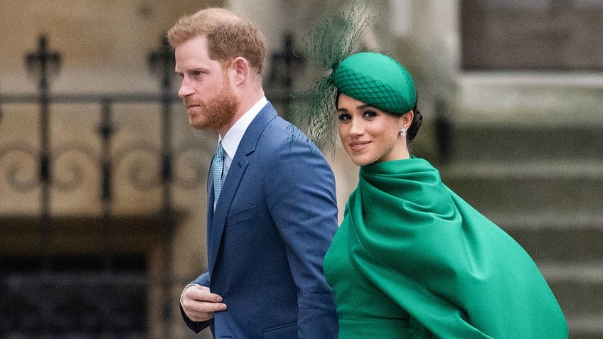 Meghan Markle wearing a green dress on the arm of Prince Harry in a blue suit.