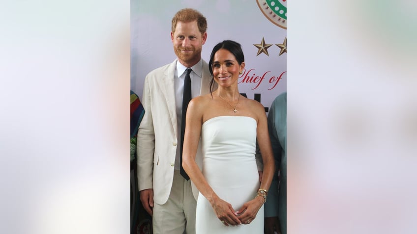Meghan Markle wearing a white tube dress standing next to Prince Harry in an ivory suit and a black skinny tie.