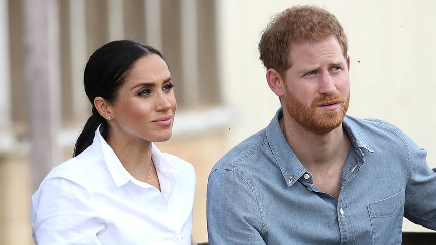 Meghan Markle wearing a white shirt and Prince Harry wearing a blue shirt looking confused