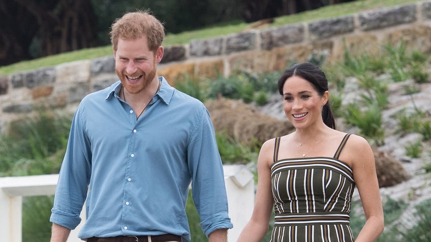 A close-up of Prince Harry in a light blue shirt and Meghan Markle in a spaghetti strap striped dress.