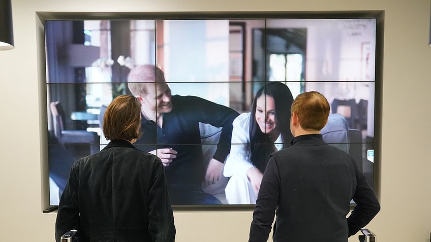 Two men watching the Duke and Duchess of Sussex laughing from their Netflix special.