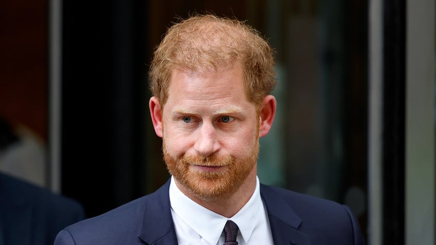 A close-up of Prince Harry wearing a navy suit and tie and looking serious