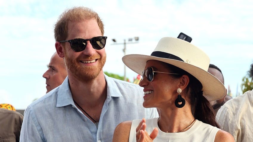 Prince Harry and Meghan Markle wearing sunglasses and smiling