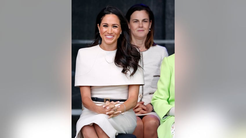 Samantha Cohen looking over a smiling Meghan Markle.