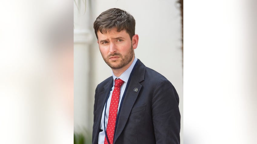 Jason Knauf wearing a dark suit and a red tie.