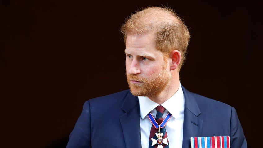 Prince Harry looking to the side in a navy suit adorned with medals.