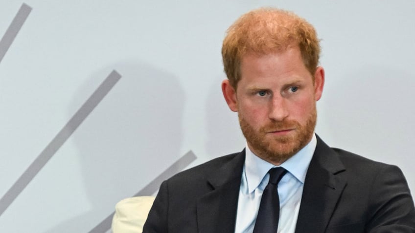 A close-up of Prince Harry wearing a dark suit and sitting on an ivory sofa