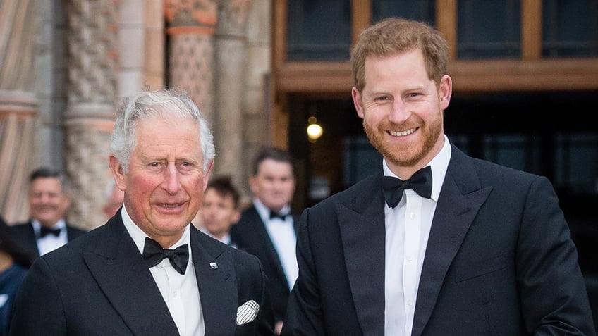 Prince Harry and King Charles standing together and smiling in matching tuxes.