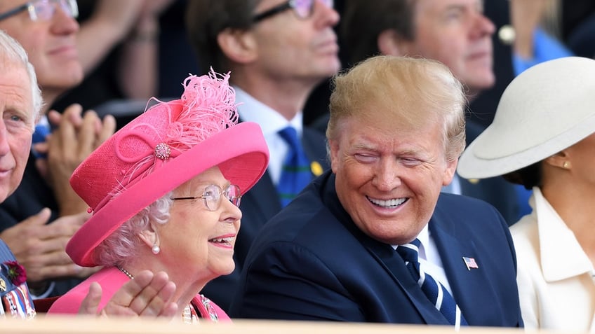 Donald Trump smiling as he sits next to Queen Elizabeth II wearing a pink coat and matching hat.