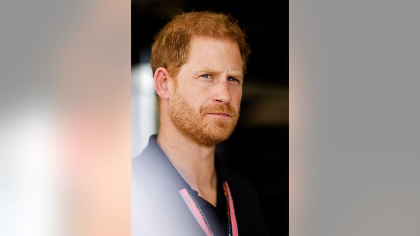 A close-up of Prince Harry looking pensive in a blue polo shirt.