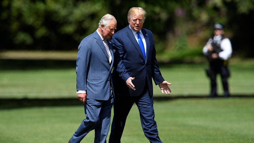 Donald Trump walking alongside the former Prince Charles in a field as they chat wearing suits.