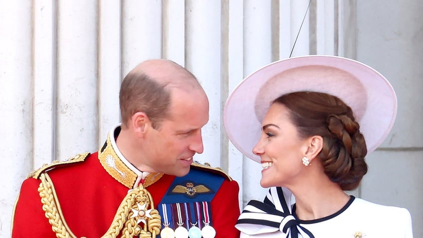 Prince William in a red uniform with medals looking adoringly at Kate Middleton