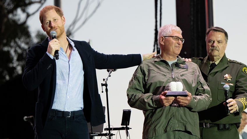 Prince Harry holding a mic and patting on the shoulder of a first responder