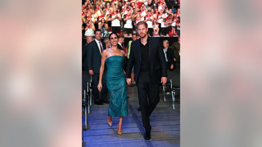 Meghan Markle wearing a teal strapless dress next to Prince Harry in a dark suit walking together