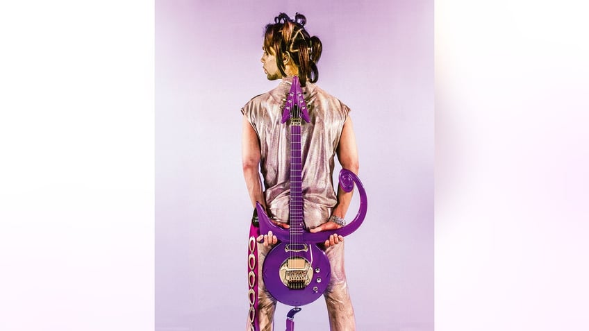 Prince with his back turned holding a guitar.