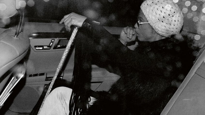 Prince holding a cane and sitting in a car.