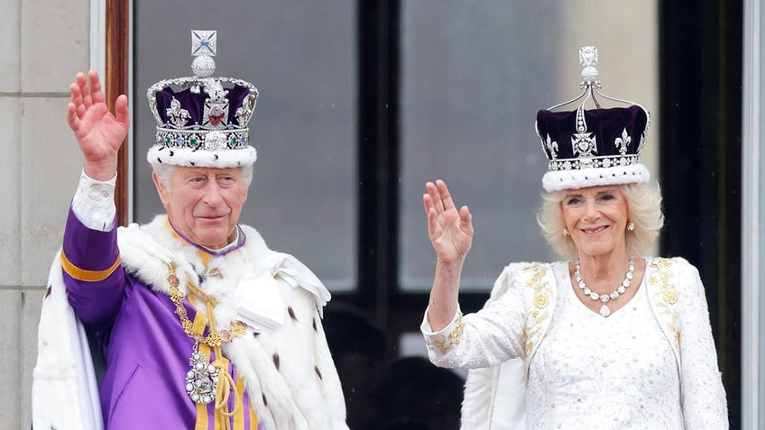 King Charles and Queen Camilla waving to the crowd while wearing robes and crowns.