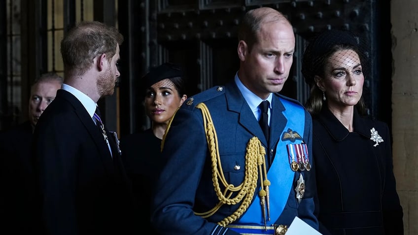 Prince Harry and Meghan Markle look at each other as Prince William and Kate Middleton look somber and walk ahead in formal wear.