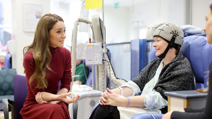 Kate Middleton wearing a burgundy dress sitting next to a cancer patient.