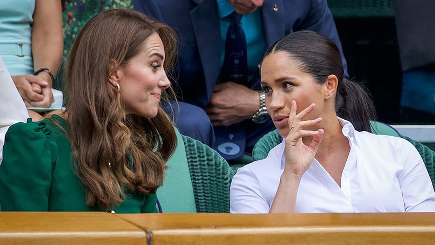 Meghan Markle and Kate Middleton sitting next to each other and chatting.