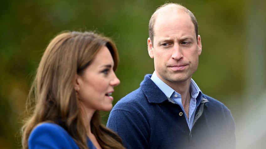 Prince William in a blue sweater looks down at wife Kate Middleton in blue as she speaks