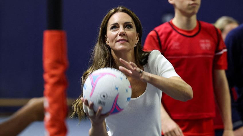 Kate Middleton holding volleyball while playing in a white t-shirt.