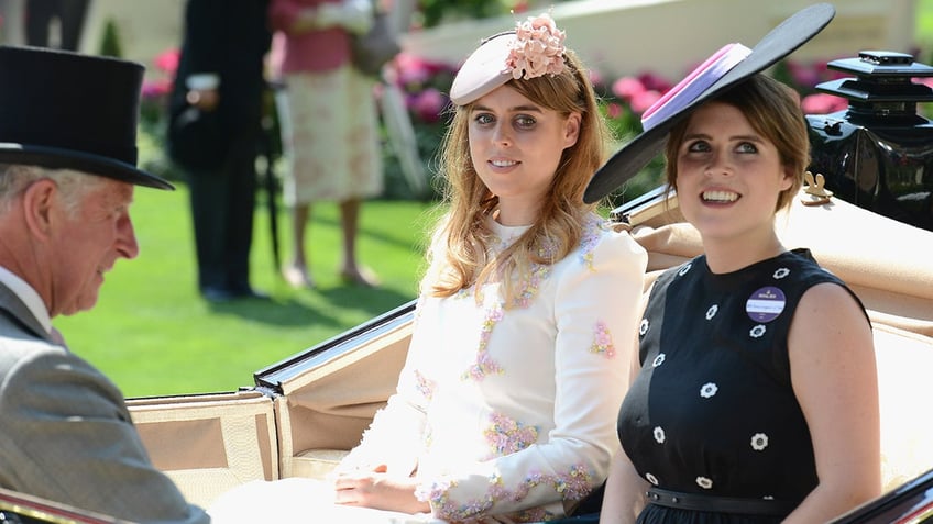 Princess Eugenie and Princess Beatrice sitting in a royal carriage with their uncle King Charles in formal wear.