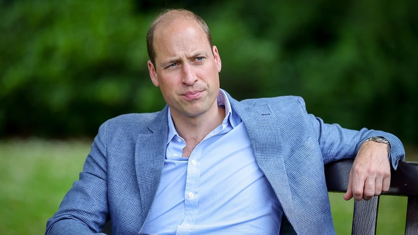 Prince William wearing a light blue blazer and a matching button down shirt looking pensive.