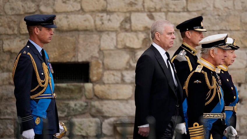 Prince William in uniform standing behind Prince Andrew in a suit and King Charles and Princess Anne in uniform.